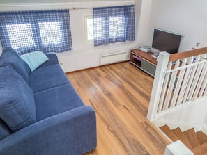 Een woonkamer met een blauwe bank, een televisie en een trap.
