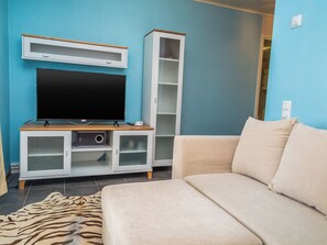 Un salon avec un téléviseur posé sur un meuble en bois, un canapé beige et un buffet blanc aux portes vitrées.