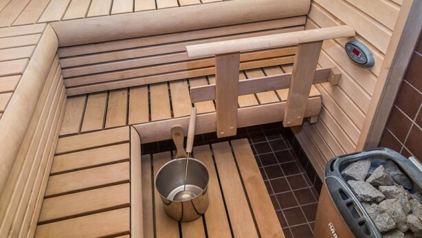 A sauna with wooden benches, a metal basin, and a control panel.
