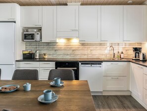 Una cocina moderna con armarios blancos, microondas, cafetera y lavavajillas.