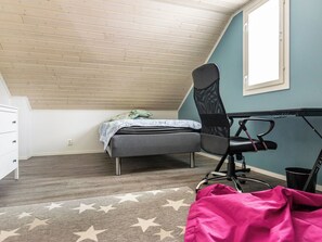 Un dormitorio con techo inclinado, una cama, un escritorio, una silla y una alfombra con estampado de estrellas.