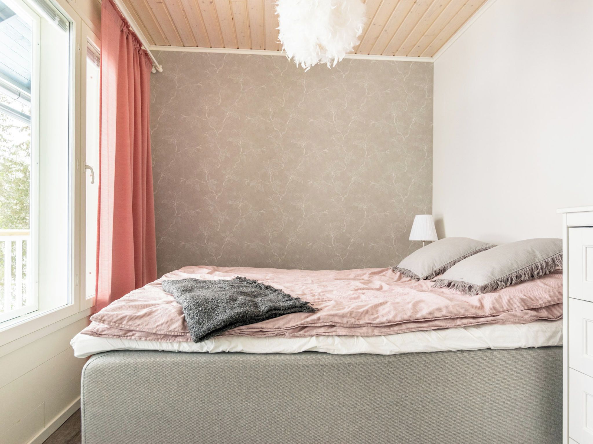 Ein Schlafzimmer mit einem Bett, einem Fenster mit Vorhängen, einer Lampe und einer Wand mit einer strukturierten Oberfläche.