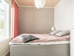 A bedroom with a bed, a window with curtains, a lamp, and a wall with a textured pattern. - Pihlajaranta by Interhome (Rautalampi)