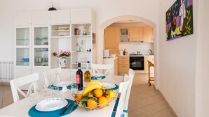 Een eetgedeelte met een tafel gedekt voor vier personen, een keuken op de achtergrond en een kleurrijk schilderij aan de muur.