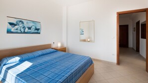 Een slaapkamer met een bed, nachtkastje, spiegel aan de muur en een deur naar een andere kamer.