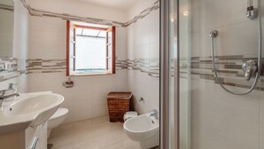 Een moderne badkamer met twee wastafels, een toiletbril, een douche met glazen wanden en een klein raam.