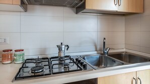 Een keuken met een gasfornuis, twee roestvrijstalen spoelbakken en houten keukenkastjes.