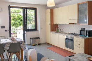 A compact kitchen with a gas stove, oven, and microwave. There is a dining table with chairs and a small trash bin.