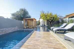 A swimming pool with a wooden deck, lounge chairs, and a small wooden structure.