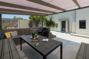 An outdoor patio with a grill, seating area, and a table with food and a book.