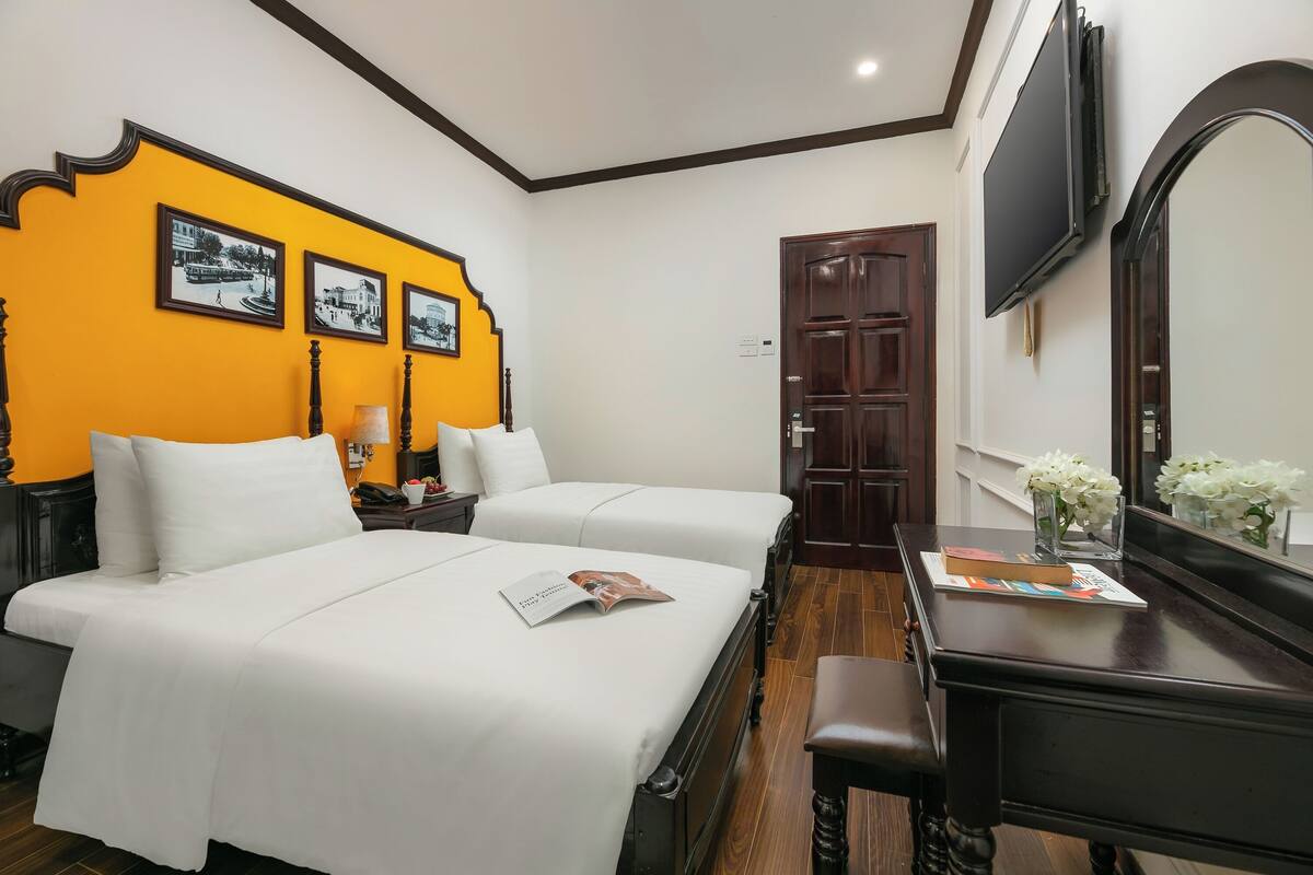 A hotel room with two beds, a wooden desk, a mirror, and a TV.