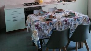 Eine kompakte Küche mit weißen Schränken, einem Gasherd, einem Spülbecken und einem Esstisch für vier Personen.