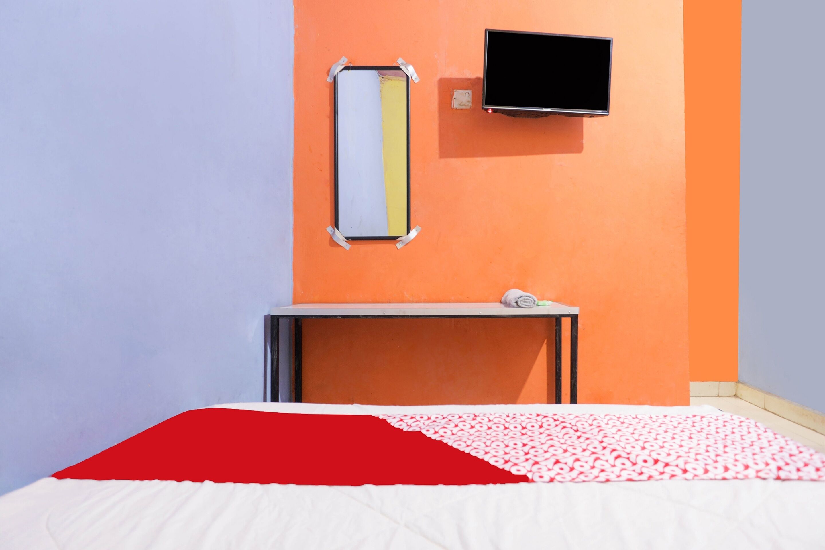 A hotel room with a bed, a TV mounted on the wall, and a small table with a towel.