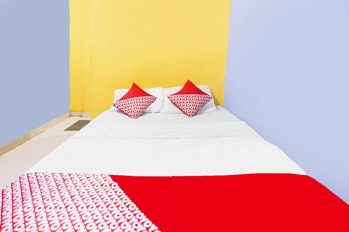 A bed with white bedding and red pillows, a red and white patterned blanket, and a yellow wall.