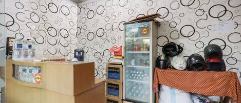 A room with a wooden reception desk, a refrigerator stocked with beverages, and a table with helmets.