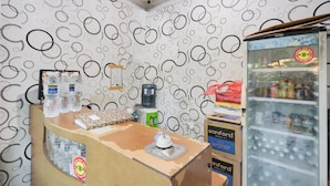 A room with a patterned wall, a counter with bottled water, a refrigerator stocked with canned goods, and a box labeled 'Sanford Water'. - SPOT ON 91887 Penginapan Rindu (Batam)