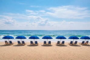 Une plage bordée de rangées de parasols bleus et de chaises longues, toutes orientées vers l’océan.