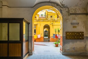 Un pasillo interior con un arco que da a un edificio amarillo, un armario de madera y un buzón.