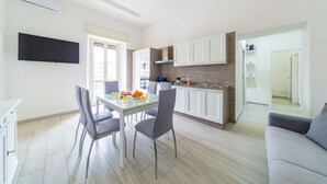 Une cuisine moderne avec des meubles blancs, une table à manger avec des chaises et un téléviseur à écran plat fixé au mur.