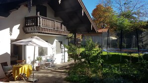 Une maison à deux étages avec un balcon, un patio couvert comprenant une table et des chaises, et un jardin avec un trampoline.