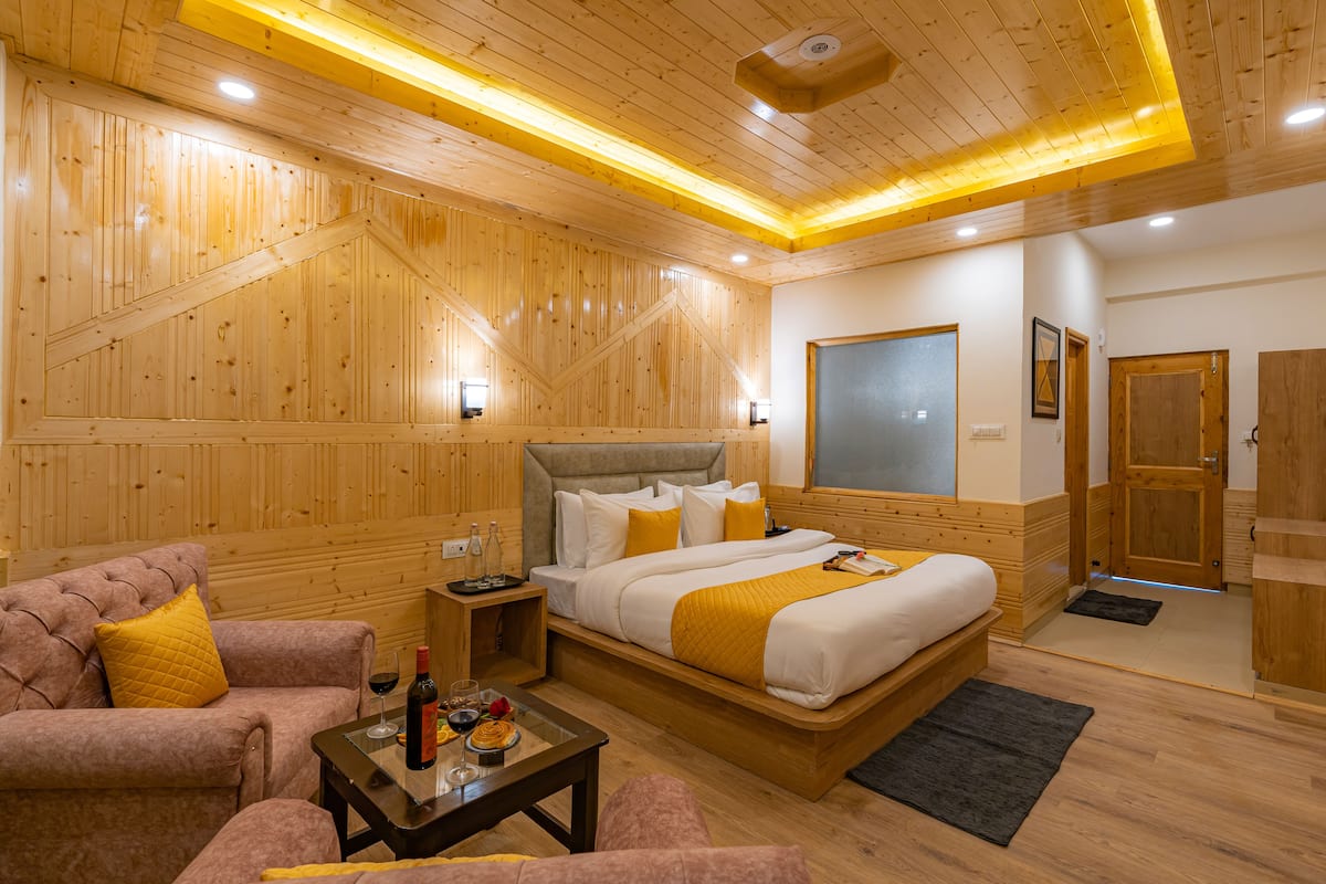 A wooden-themed hotel room with a large bed, a sofa, a coffee table, and a wooden wardrobe.