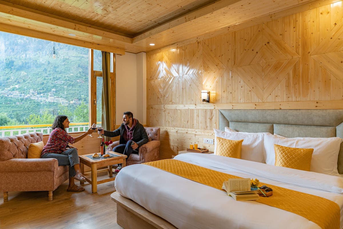 A cozy hotel room with a large bed, a sofa, and a view of a mountainous landscape.