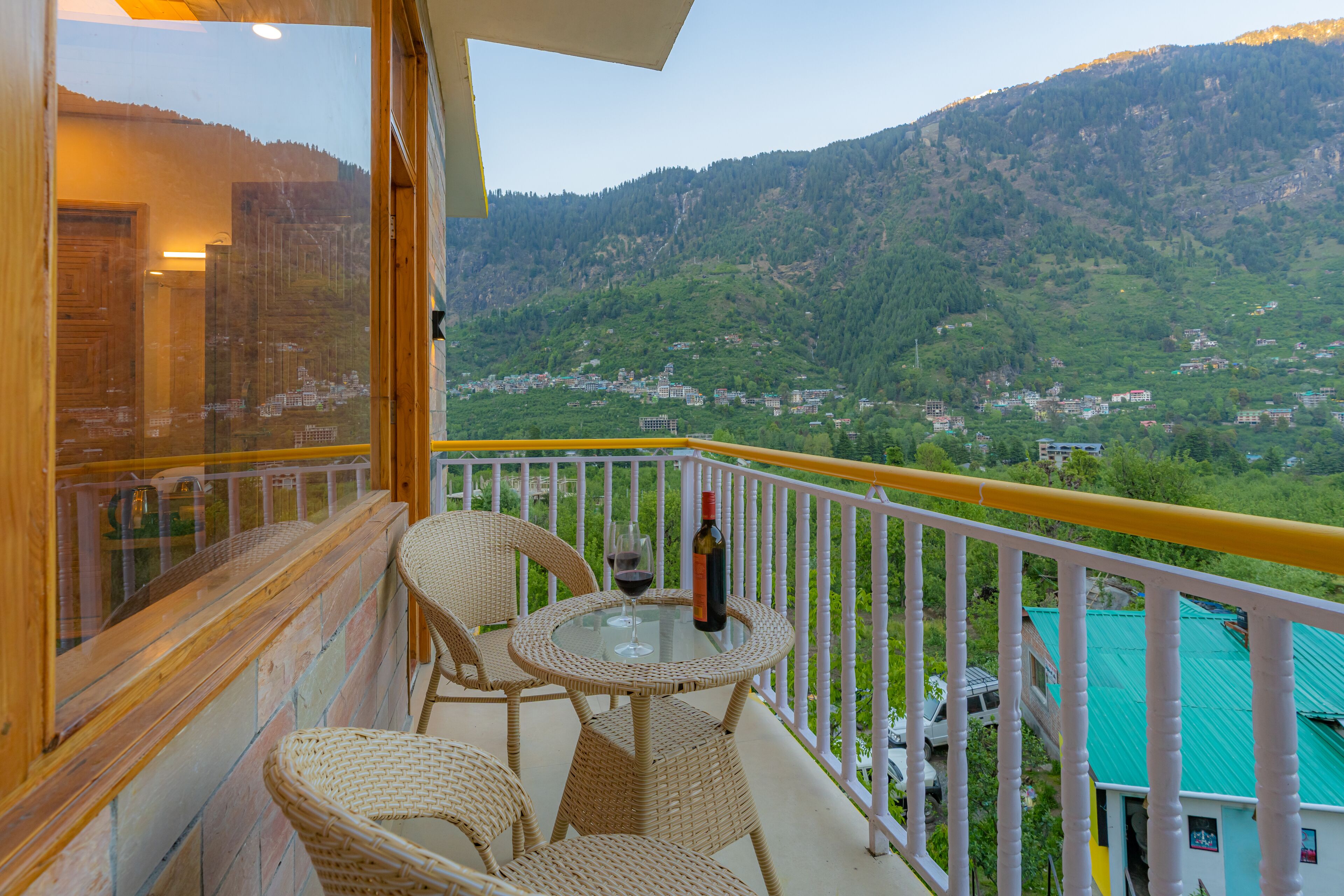 A balcony with wicker chairs and a table, overlooking a mountainous landscape.