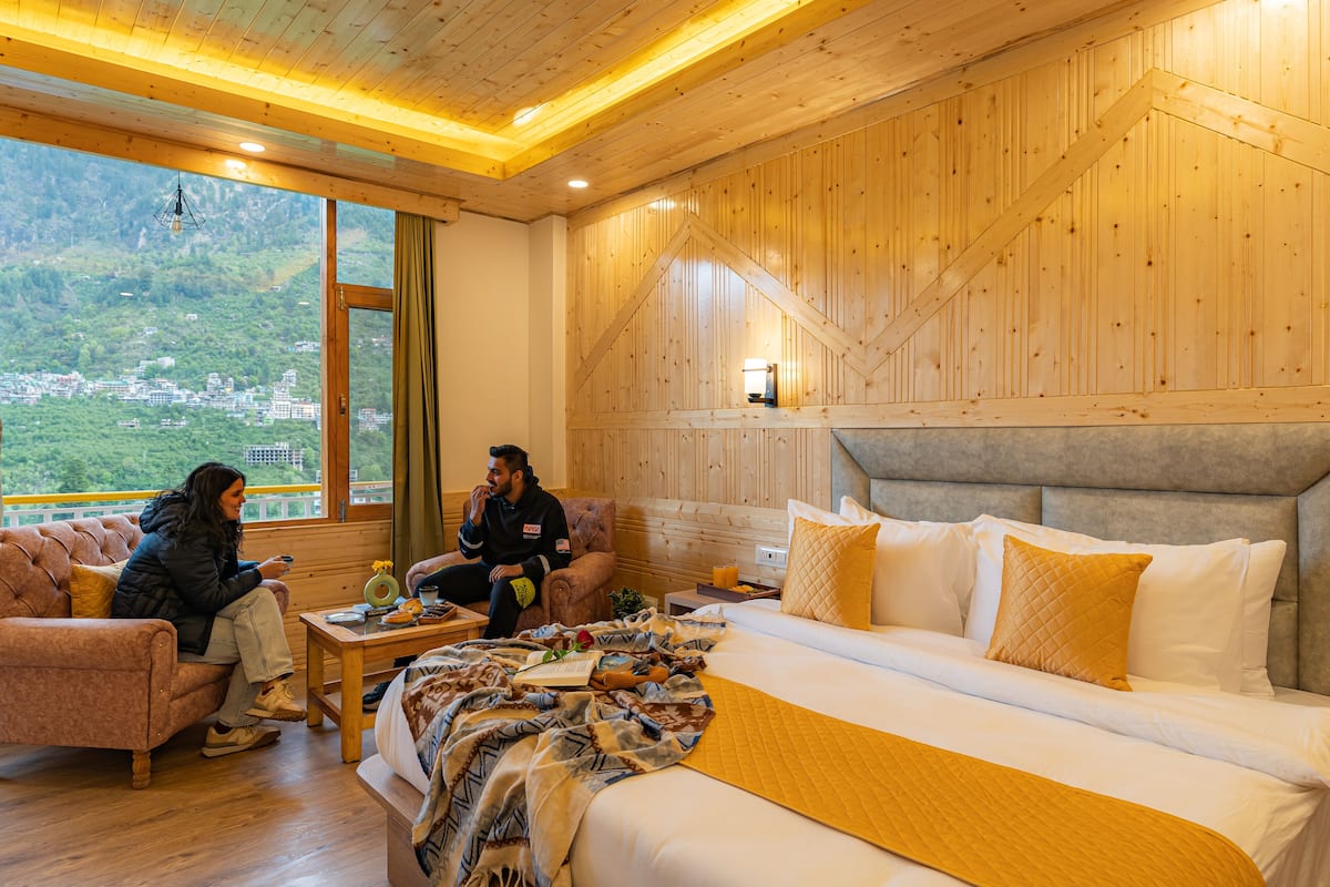 A hotel room with a large bed, a sofa, and a view of a mountainous landscape.