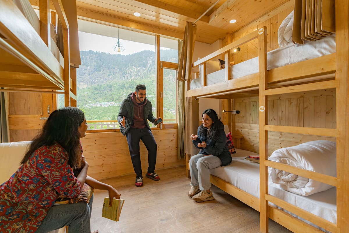 A wooden cabin with bunk beds, a window with a mountain view, and a person standing near the window.