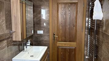 A modern bathroom with a wooden vanity, a large mirror, a glass shower enclosure, and a towel rack.