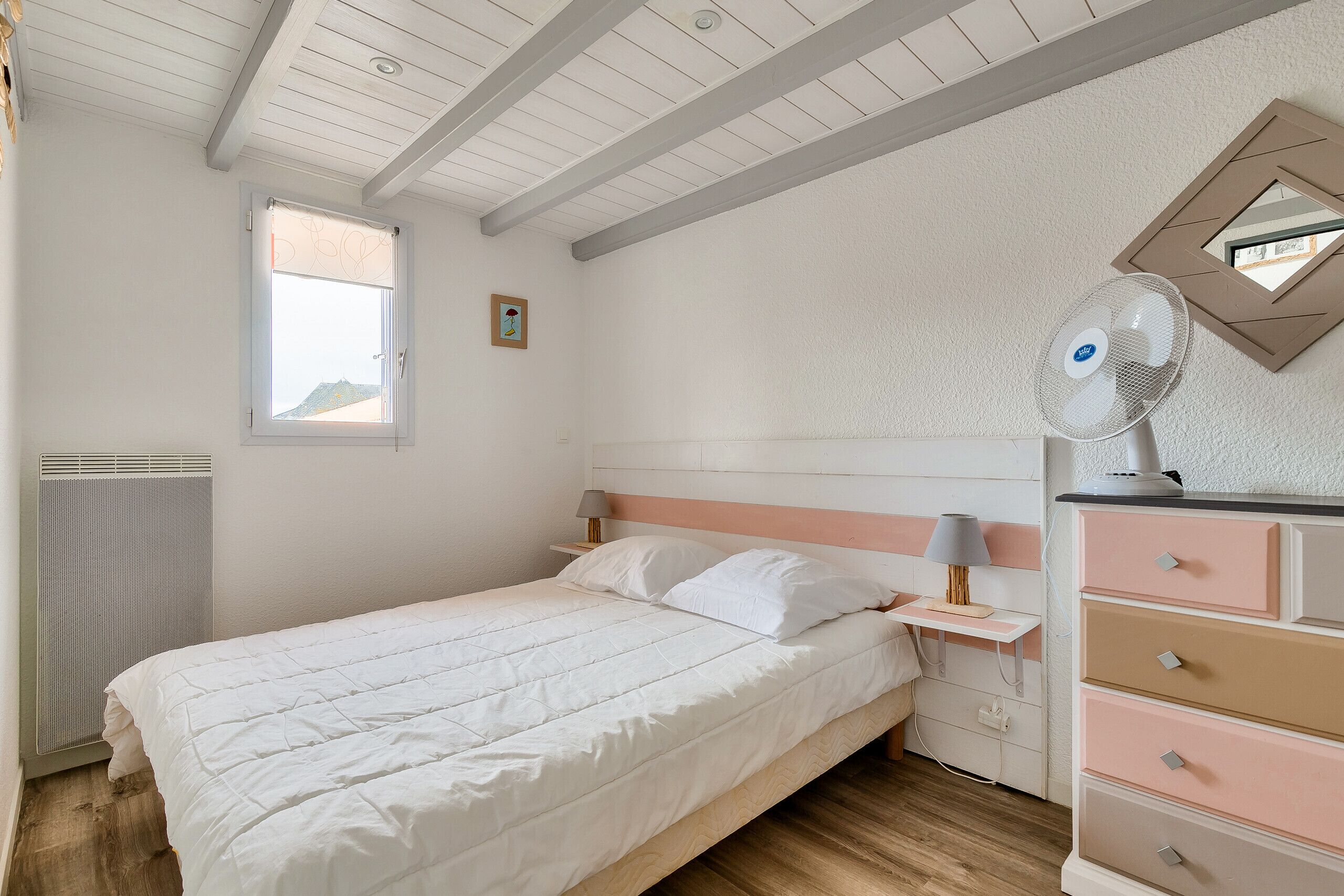 Een slaapkamer met een bed, een dressoir, een nachtkastje, een raam en een radiator.