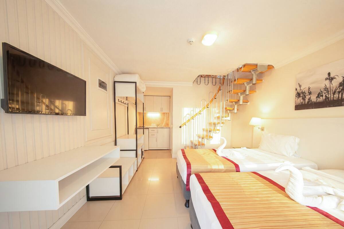 A hotel room with a bed, a TV, a kitchen area, and a staircase.