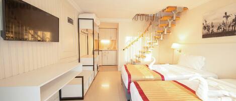 A hotel room with a bed, a TV, a kitchen area, and a staircase.