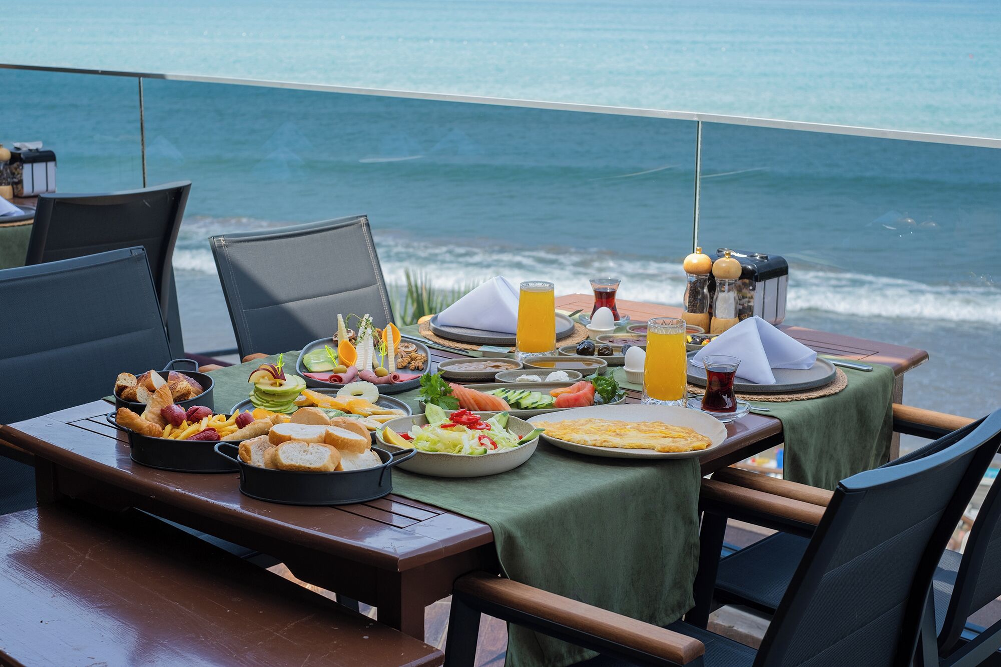 Una mesa con diversos alimentos para el desayuno, como pan, queso y frutas, con vista al mar.