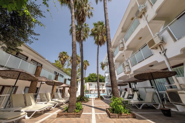 Un resort con zona de piscina, tumbonas, palmeras y un edificio moderno equipado con aire acondicionado.