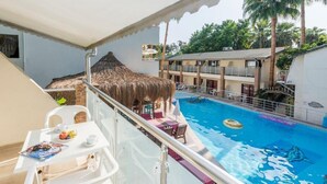 A balcony with a pool, a table with a magazine, and a thatched roof structure. - Tropic Beach Club Side  (Manavgat)