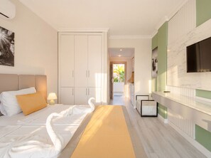 A bedroom with a bed, a wardrobe, a TV, and a hallway leading to a balcony.