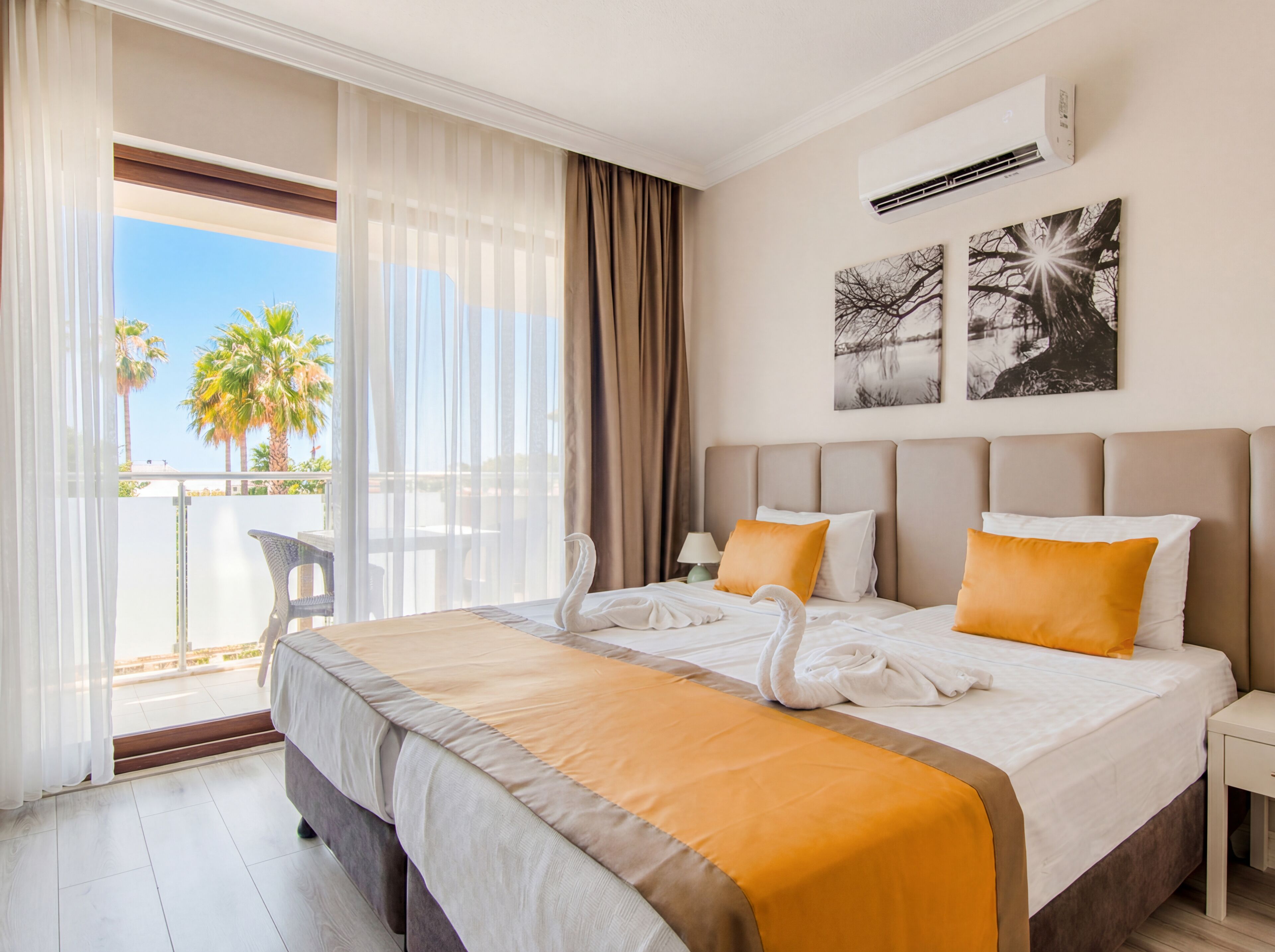 Una habitación de hotel con cama, balcón y vistas a palmeras, y un equipo de aire acondicionado en la pared.