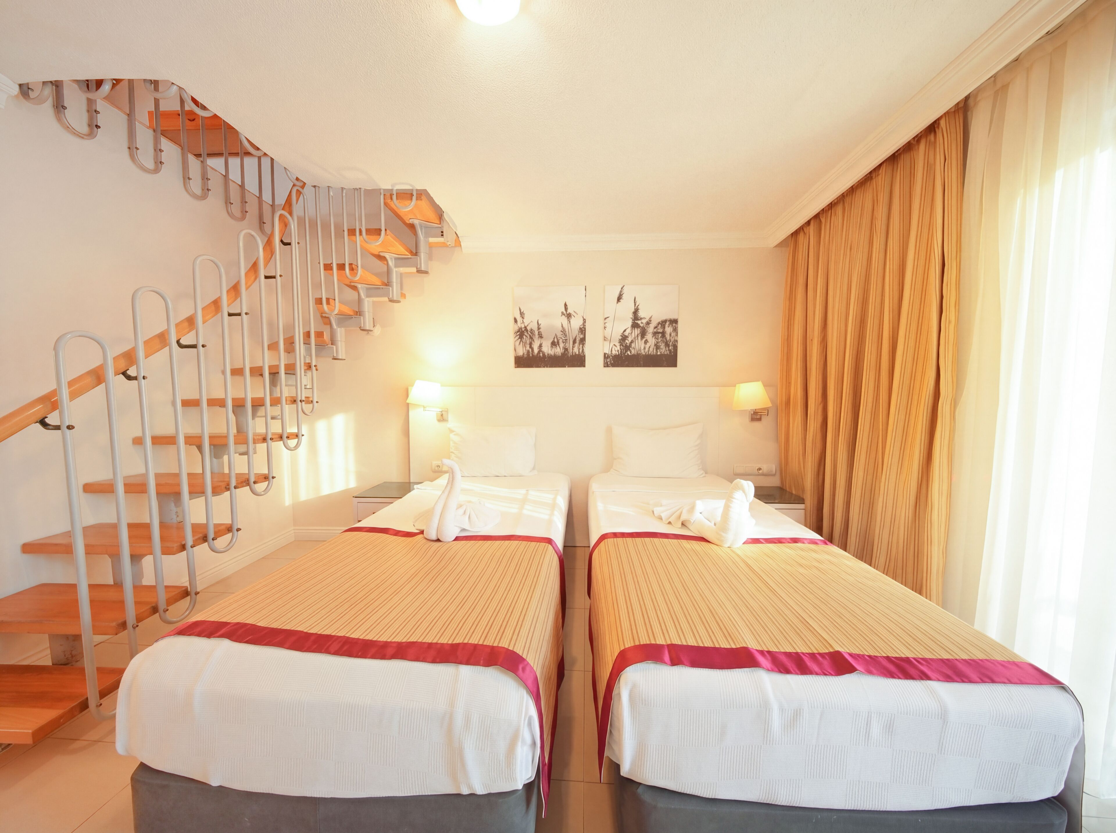 A hotel room with two beds, a staircase, and a view of the outside.