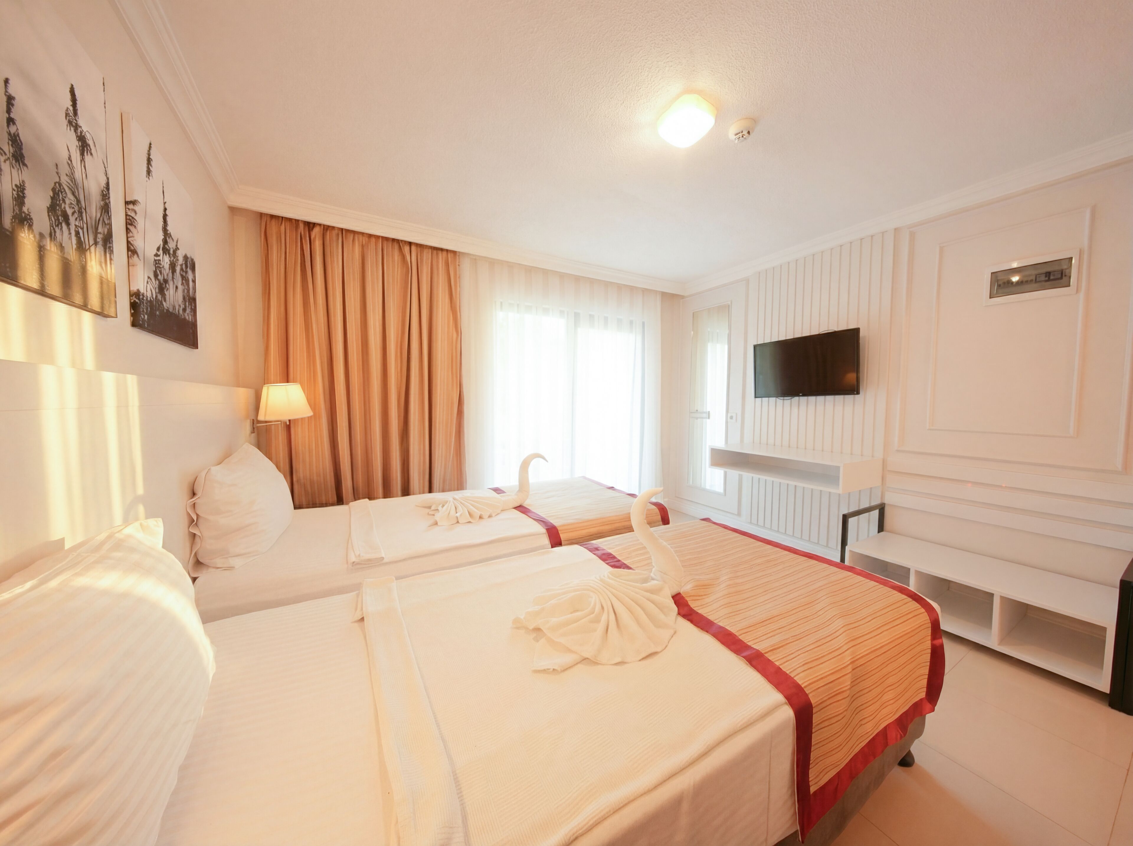 A hotel room with two beds, a TV, and a window with curtains.