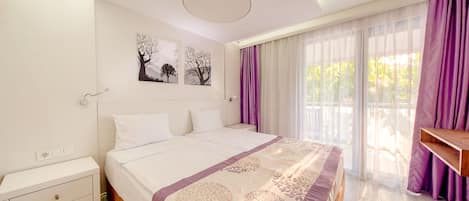 A bedroom with a bed, a nightstand, a wall-mounted light, and a window with curtains.