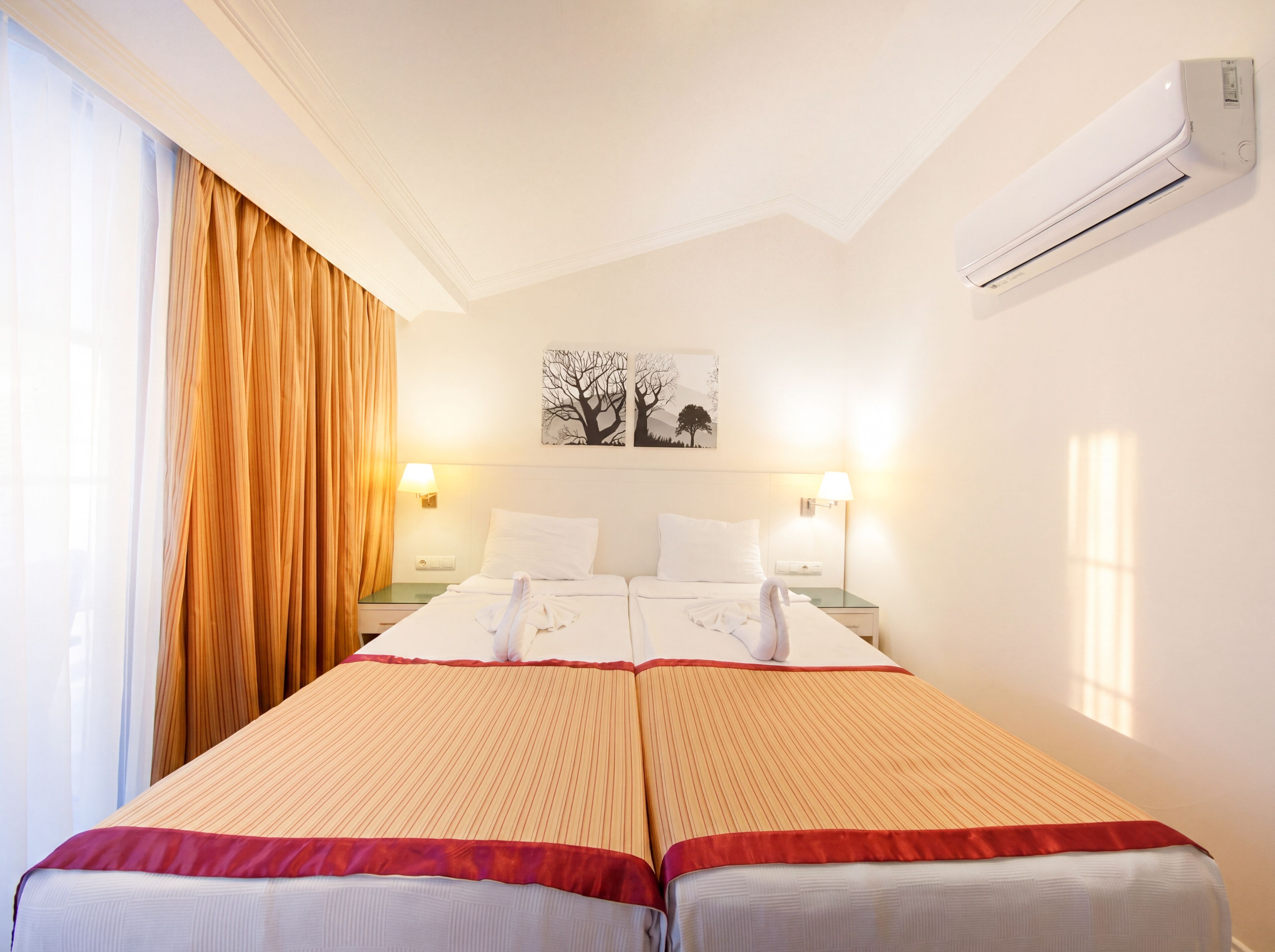 Een hotelkamer met twee bedden, een groot raam met gordijnen, een airconditioning en een kunstwerk aan de muur.