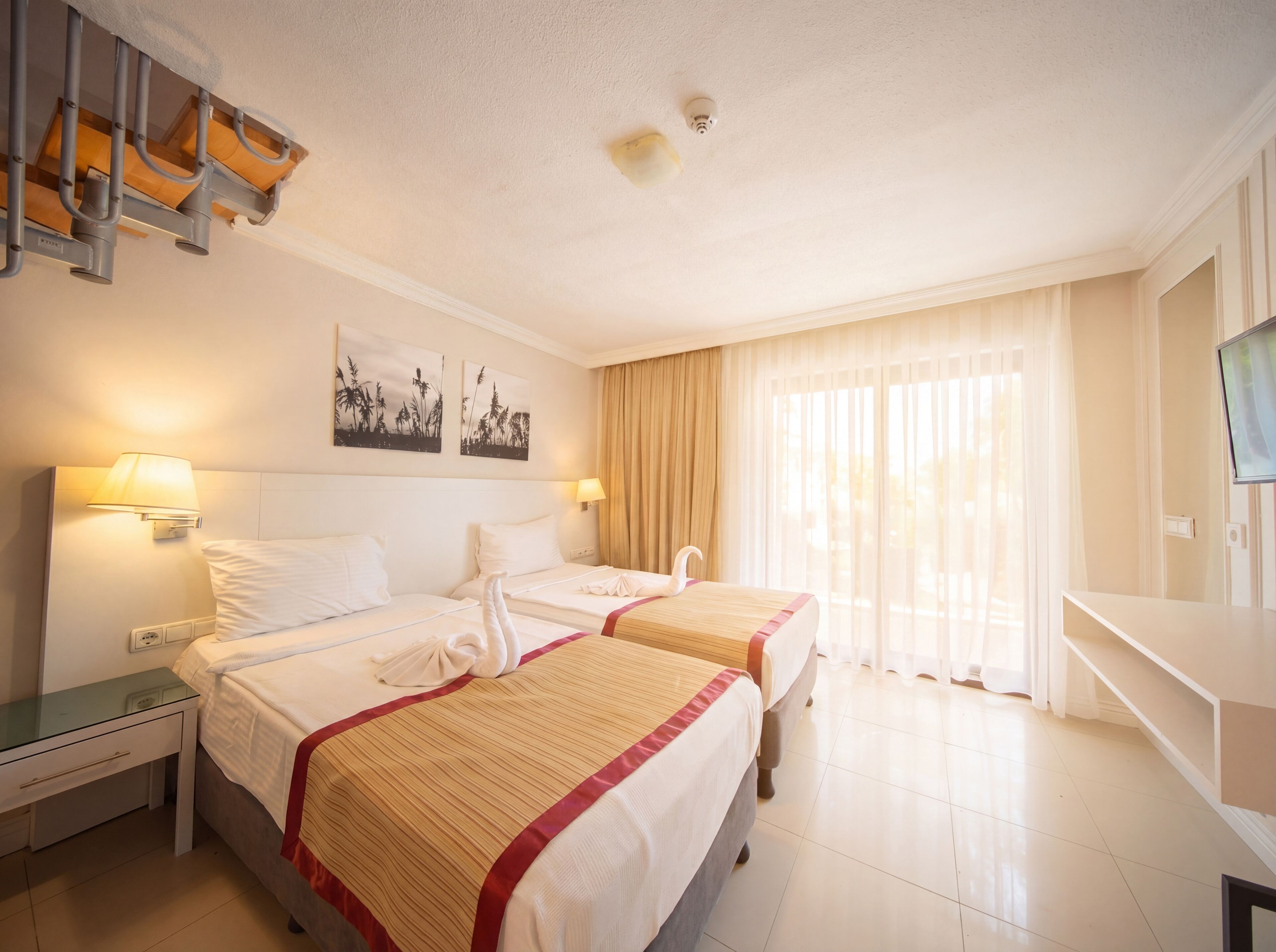 A hotel room with two beds, a desk, a TV, and a window with curtains.