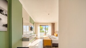 A hotel room with a bed, a TV mounted on a wall, a bench, and a view of palm trees. - Tropic Beach Club Side  (Manavgat)
