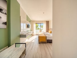 Habitación de hotel con cama, televisor montado en la pared, banca y vista a palmeras.
