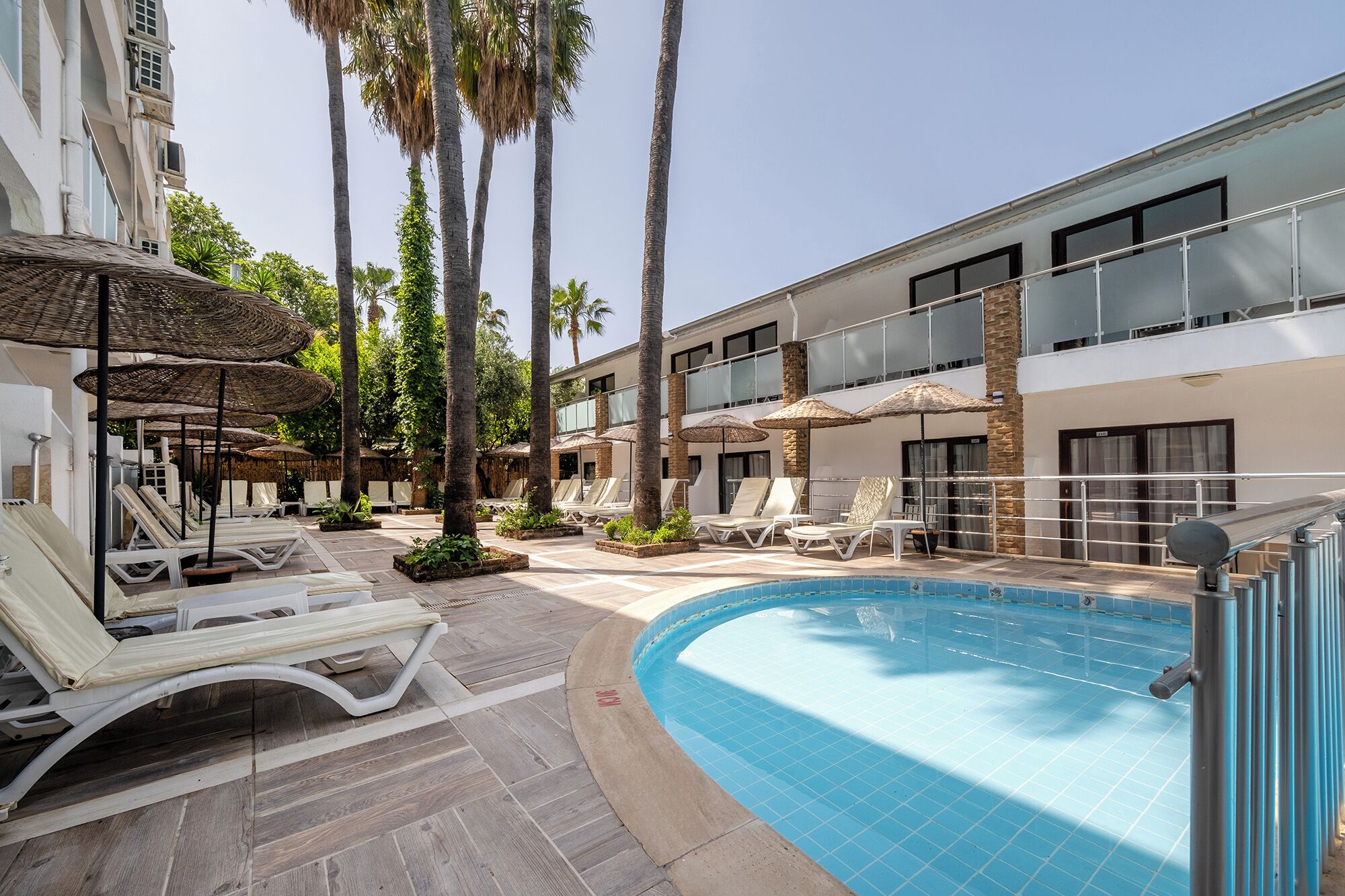 A pool area with lounge chairs and umbrellas, surrounded by palm trees and a building with balconies.