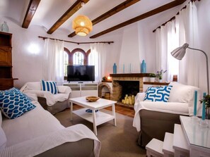 Ein gemütliches Wohnzimmer mit zwei Sofas, einem Kamin, einem Fernseher und einer Pendelleuchte.