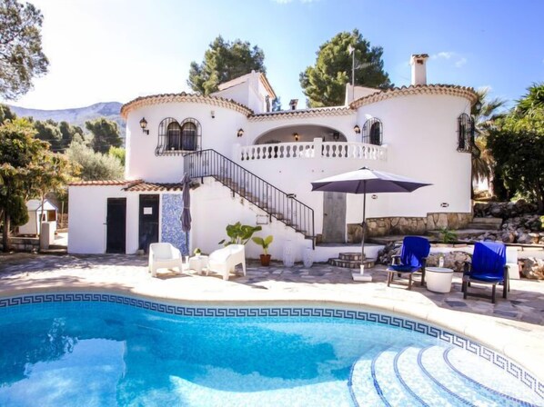 Eine Villa im mediterranen Stil mit Swimmingpool, Sitzgelegenheiten im Freien und einer Treppe zu einem Balkon.