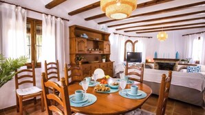 A dining area with a wooden table set for four, surrounded by wooden chairs with cushioned seats. A wooden cabinet with dishes is visible in the background. - Garoe Villa by Interhome (Dénia)