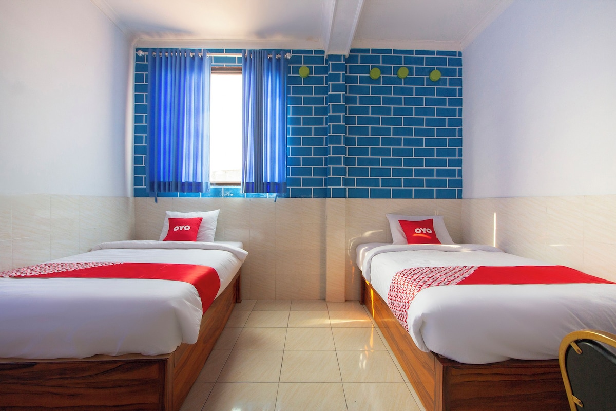 Una habitación de hotel con dos camas individuales, una ventana con cortinas azules y una pared de ladrillo azul.